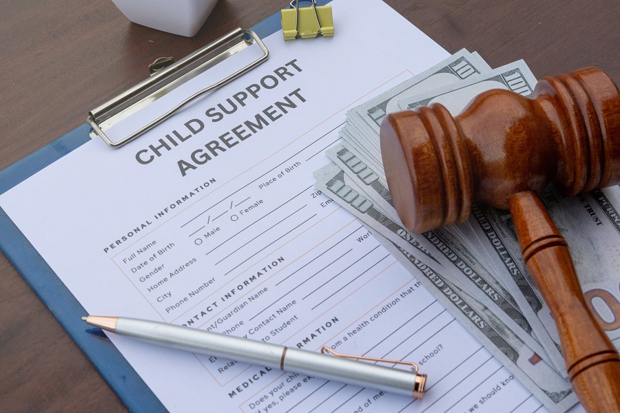 A detailed child support agreement paper on a desk with cash, a gavel, and a calculator, representing legal obligations and financial support.