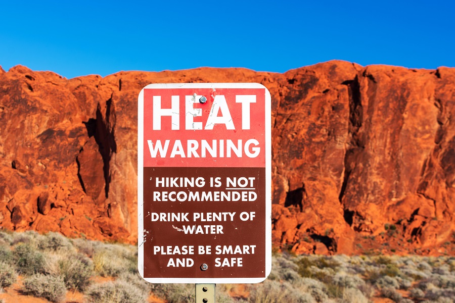 Heat warning sign informs tourists of the dangers of heat exhaustion from hiking in the desert climate. Blurred scenic red sandstone formations and desert scrub landscape background. Blue sky.