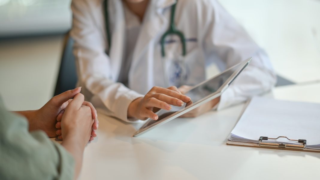 A doctor explaining something to a patient while looking at a tablet or computer