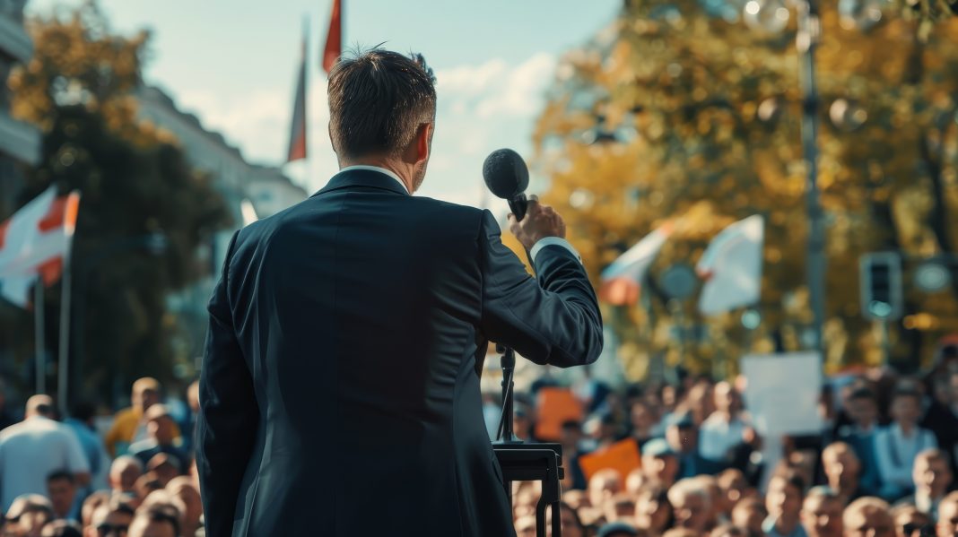 A politician gives a speech outdoors in front of a large crowd.