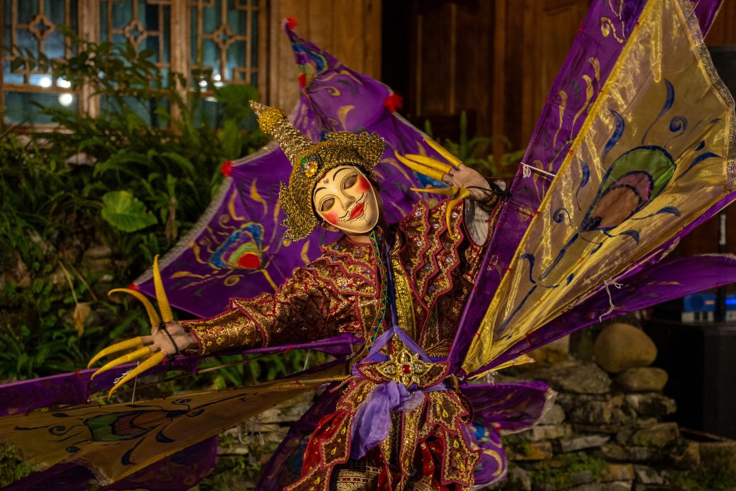 A performer in an elaborate red, gold, and purple costume with ornate embroidery and a stylized mask presents a traditional dance during Albuquerque’s Heritage Day Festival, symbolizing cultural pride and artistry.