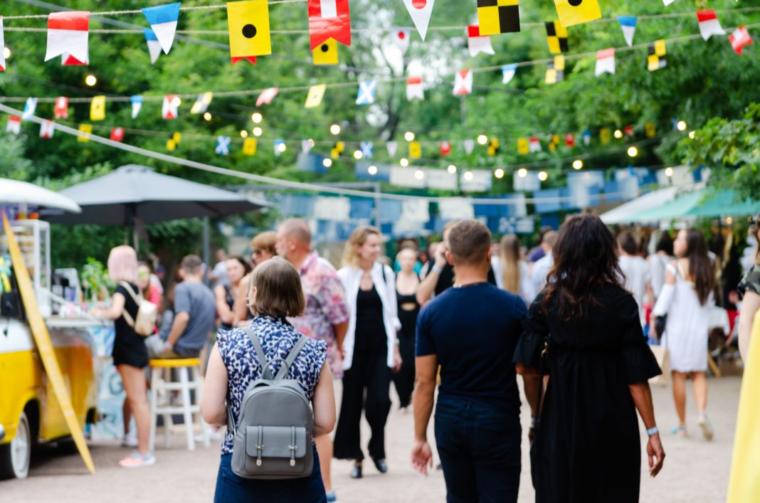 Crowds gather at a Tri-Cities outdoor festival in northwestern New Mexico, with colorful flags overhead, food stands, and families enjoying the lively atmosphere.