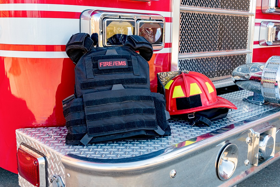 Ballistic vest and red firefighter helment on fire truck bumper. Concept of evolving role of fire department response to mass casualty shooting and terrorism