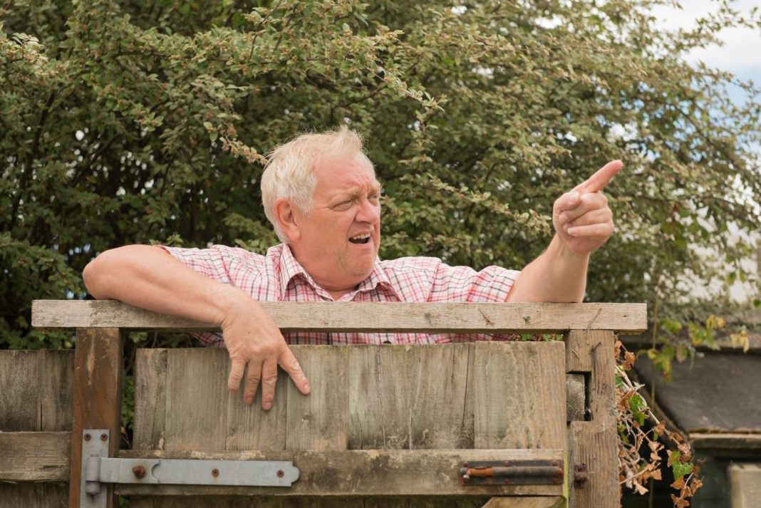 Man talking to someone over his fence.