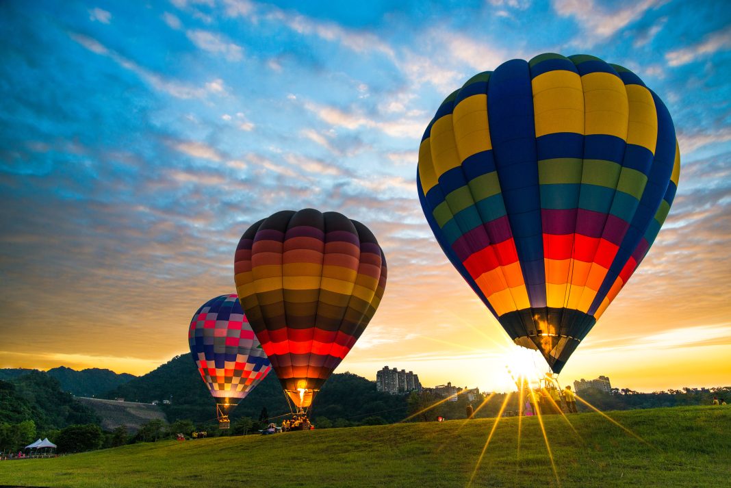 Hot air balloons rising over Albuquerque’s desert landscape during sunrise, with Rainbow Ryders leading the ascent.