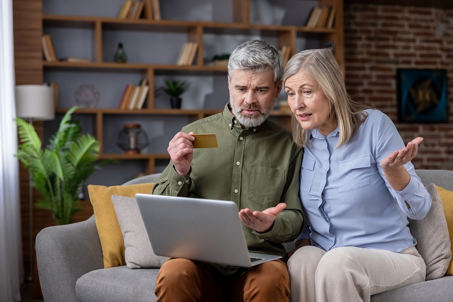 Senior couple on sofa frustrated and worried as they try to complete an online credit card payment on a laptop, highlighting confusion, security concerns and financial stress