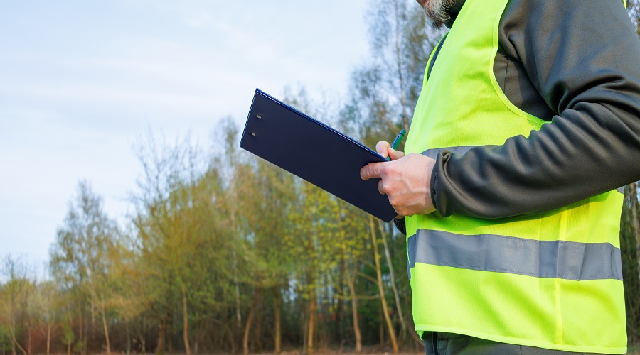 Close up male writing a report for a new construction project on a site after forest clearing. An ecologist conducts environmental monitoring and soil analysis.