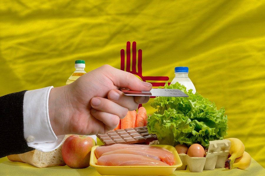 man stretching out credit card to buy food in front of complete wavy american state flag of new mexico