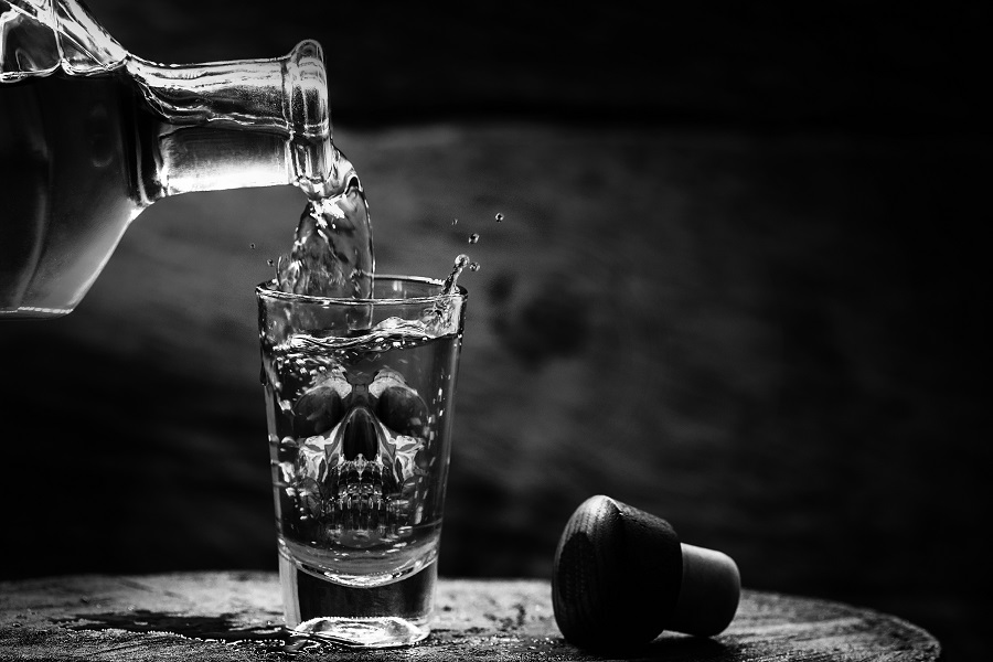 Drink bottle and glass with alcohol content. Image of translucent skull in glass. Alcoholism, addiction or poison concept.