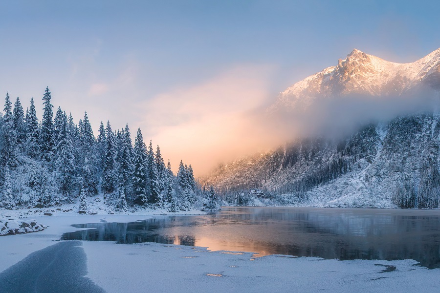 Sunrise in winter mountains. Mountain reflected in ice lake in morning sunlight. Amazing panoramic nature landscape in mountain valley.