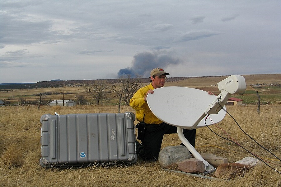 National Weather Service Incident Meteorologists (IMET) Brent Wachter aiming/positioning the Direcway satellite dish. Once positioned correctly, the IMET can then download much needed weather data. Smoke from the Ojo Felix Fire is seen in the background. New Mexico, Sangre de Cristo Mountains. 2006 April 14.