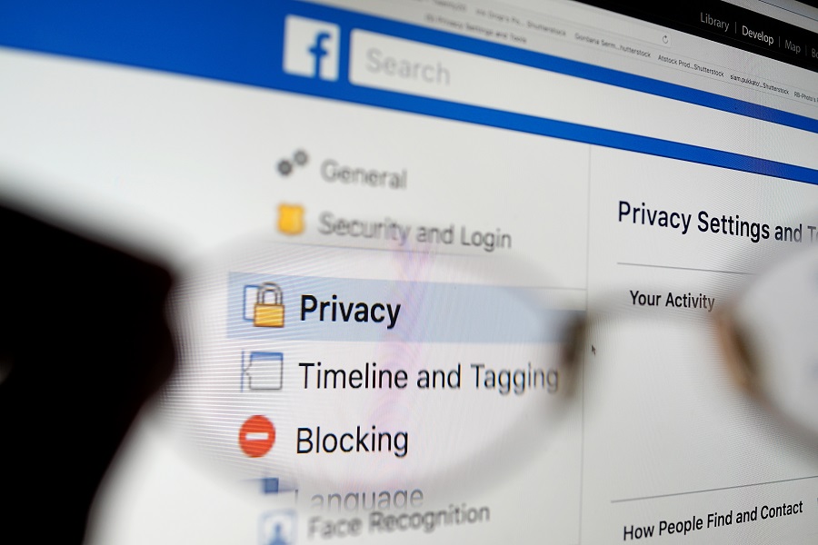 Facebook security and privacy issues. Close up hand holding an eyeglass with Facebook privacy check-up page screen as background.