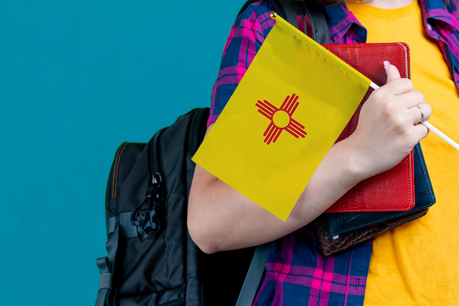 Young girl with school stuff holds in hand New Mexico flag close up